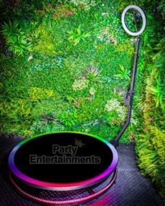 360 video booth 100cms black with rainbow lights against green fake foliage at event. Purchase a 360 Photo Booth as shown in this image