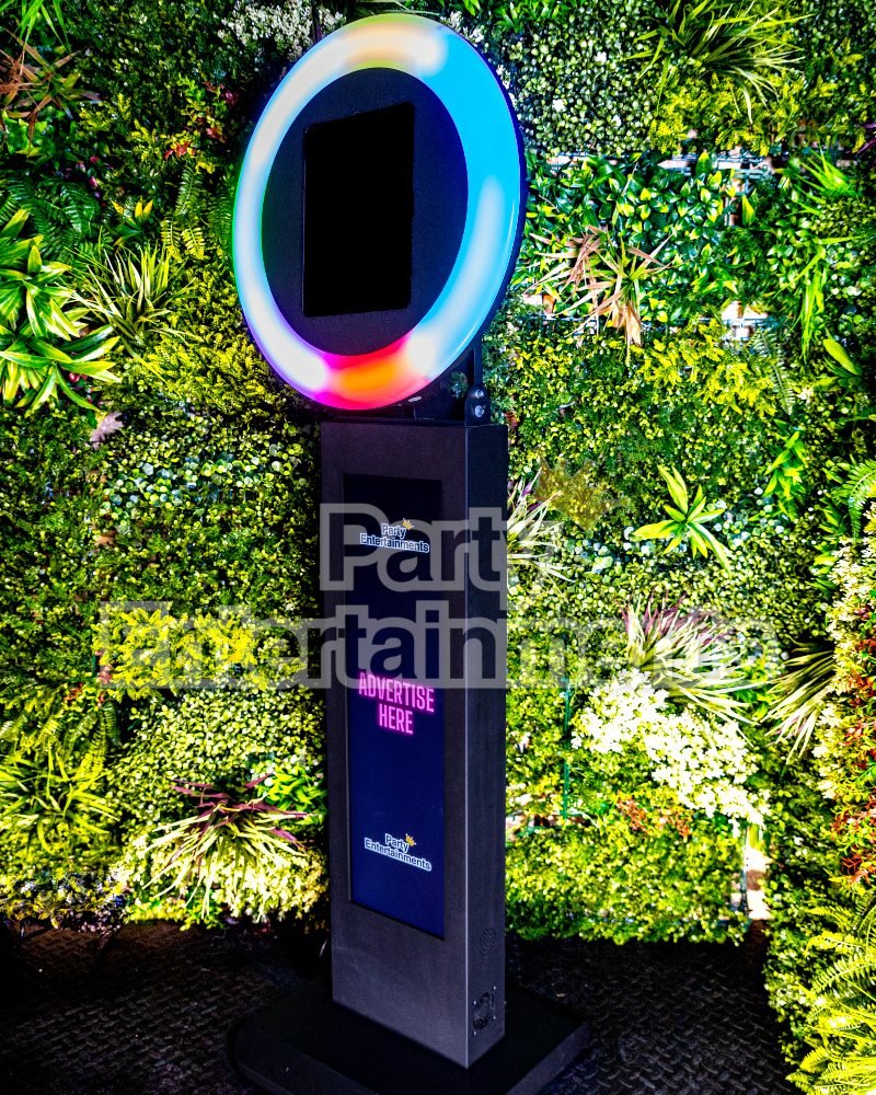 Black with multi colour iPad Selfie Photo Booths. Showing space to digitally advertise in the base. Set against flower and leaf background at event.