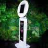 White iPad Selfie Photo Booth against a fake green leafy background at an event.